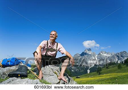 Stock Image - mature man sitting barefoot on rock in the mountains. Fotosearch