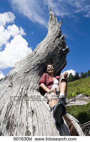 Stock Image - mature woman in the mountains relaxing on log. Fotosearch