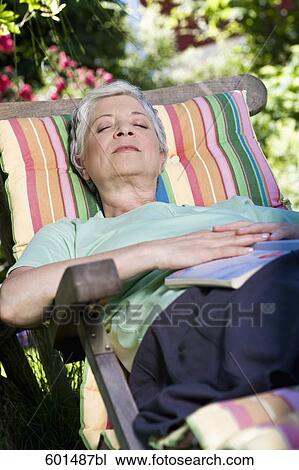 Stock Image - mature woman relaxing on deck chair in garden. Fotosearch
