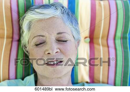Stock Image - mature woman relaxing on deck chair in garden. Fotosearch