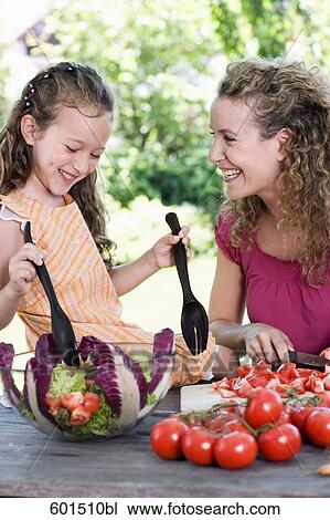 Stock Image - mother and daughter preparing salad of tomatoes in garden. Fotosearch