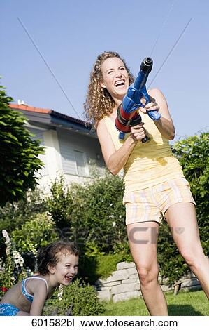 Stock Image - mother playing in garden with water pistol. Fotosearch