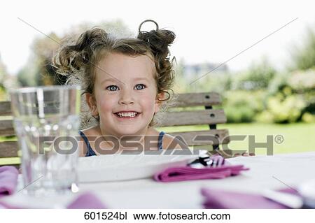 Stock Image - portrait of little girl sitting at table in garden. Fotosearch