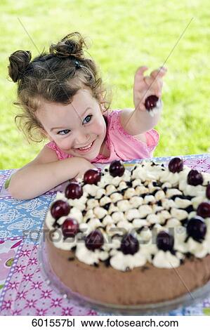 Stock Image - portrait of little girl stealing cherry from cake. Fotosearch