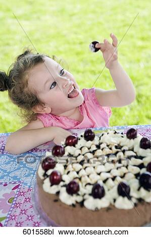 Stock Image - portrait of little girl stealing cherry from cake. Fotosearch
