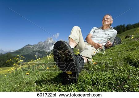 Stock Image - portrait of mature man relaxing on meadow in the mountains. Fotosearch