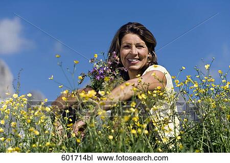 Stock Image - portrait of mature woman sitting in summer meadow. Fotosearch