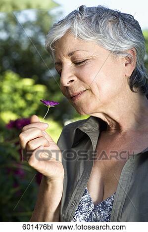 Stock Image - portrait of mature woman smelling flower. Fotosearch