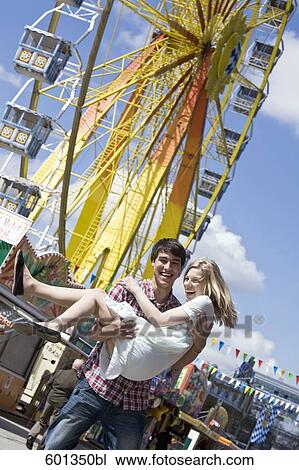 Stock Image - portrait of teenage boy carrying his girlfriend at fun fair. Fotosearch