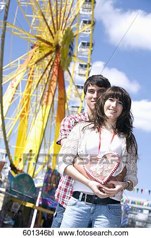 Stock Image - portrait of teenage couple with gingerbread heart at fun fair. Fotosearch