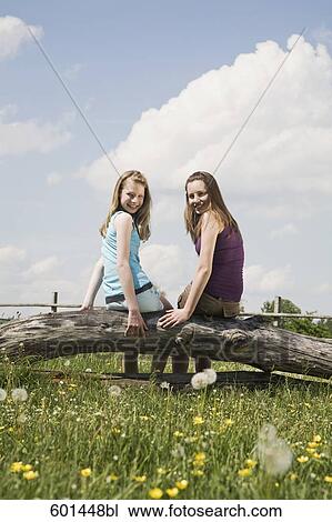 Stock Image - portrait of two girls sitting on tree trunk at horse ranch. Fotosearch