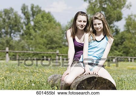Stock Image - portrait of two girls sitting on tree trunk together. Fotosearch
