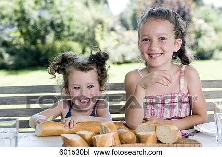 portrait of two little sisters sharing bread at table in garden View Large Photo Image Stock Image - portrait of two little sisters sharing bread at table in garden. Fotosearch