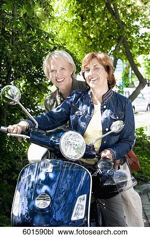 Stock Image - portrait of two senior woman sitting on scooter. Fotosearch