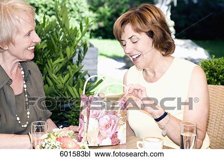 Stock Image - portrait of two senior women in cafe one opening present. Fotosearch