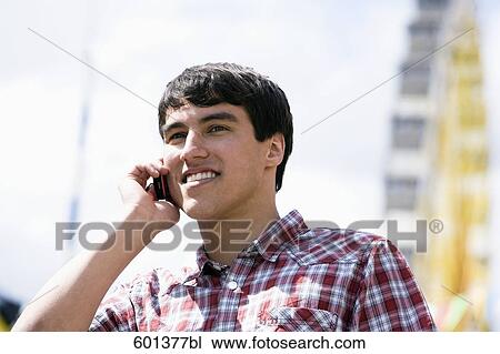 Stock Image - portrait of young man talking on mobile phone at fun fair. Fotosearch