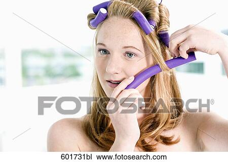 Stock Image - portrait of young woman putting curlers in her hair. Fotosearch