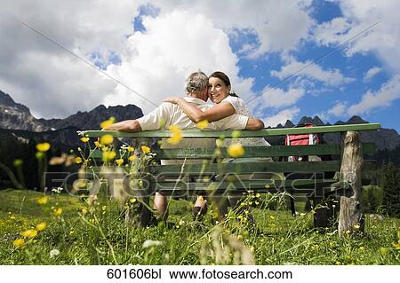 Stock Image - rear view of mature couple sitting on bench in front of mountains. Fotosearch