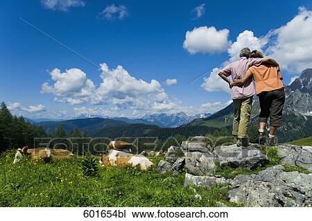 Stock Image - rear view of mature couple standing in embrace in the mountains. Fotosearch