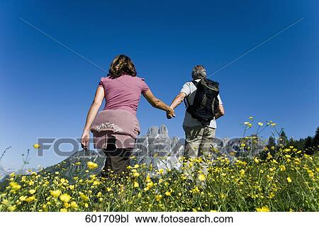 Stock Image - rear view of mature couple walking hand in hand in the mountains. Fotosearch