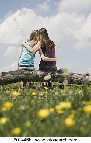 rear view of two girls sitting on tree trunk embracing each other View Large Photo Image Stock Image - rear view of two girls sitting on tree trunk embracing each other. Fotosearch