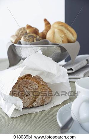 Stock Image - still life of fresh bun in paper bag on breakfast table. Fotosearch