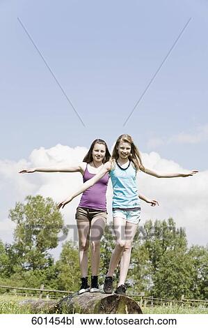 Stock Image - two girls balancing on tree trunk. Fotosearch