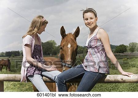 Stock Image - two girls sitting on fence at horse ranch. Fotosearch