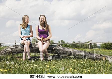 two girls sitting together on tree trunk at horse ranch View Large Photo Image Stock Image - two girls sitting together on tree trunk at horse ranch. Fotosearch