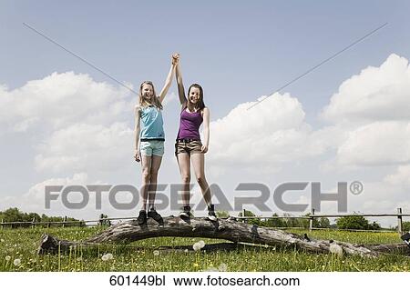 two girls standing on tree trunk raising arms together View Large Photo Image Stock Image - two girls standing on tree trunk raising arms together. Fotosearch