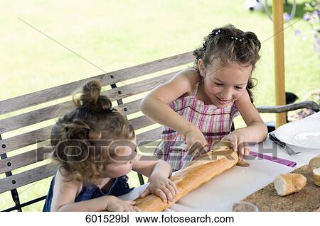 Stock Image - two little sisters sharing bread at table in garden. Fotosearch