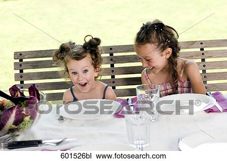 two little sisters sitting at table in garden having fun View Large Photo Image Stock Image - two little sisters sitting at table in garden having fun. Fotosearch