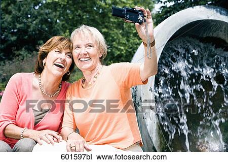Stock Image - two senior women taking self-portrait with digital camera. Fotosearch