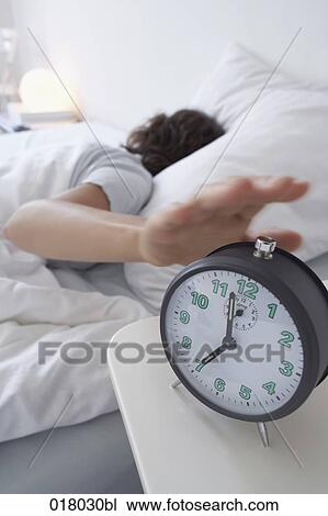 Stock Image - woman sleeping in bed switching off alarm clock. Fotosearch