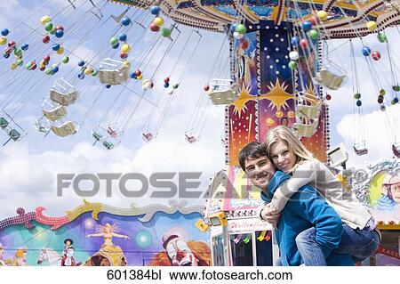 Stock Image - young man giving girlfriend piggyback ride at fun fair. Fotosearch