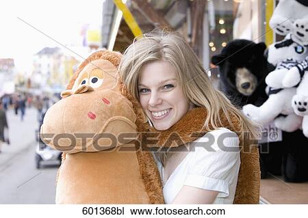 Stock Image - young woman at fun fair holding cuddly toy. Fotosearch
