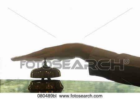 Stock Image - back lit close-up of female hand ringing hotel reception bell. Fotosearch