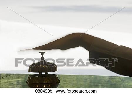 Stock Image - back lit close-up of female hand ringing hotel reception bell. Fotosearch