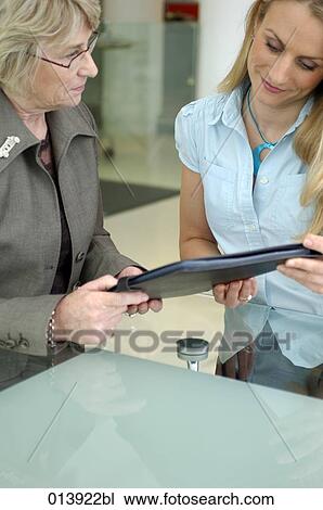 Stock Image - blond executive presenting file to elderly businesswoman. Fotosearch
