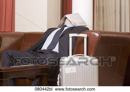Stock Image - businessman dozing in hotel lobby with newspaper covering his face. Fotosearch