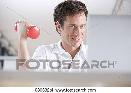 Stock Image - businessman exercising with dumb bell while sitting at laptop computer. Fotosearch