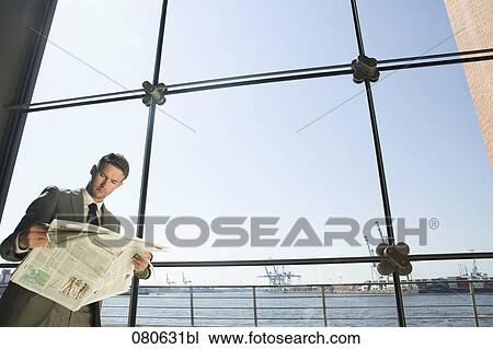 Stock Image - businessman reading newspaper in front of window. Fotosearch