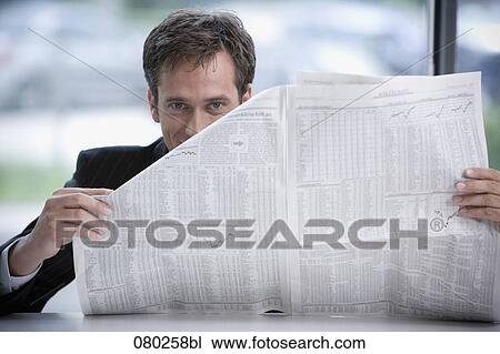 Stock Image - businessman sitting at desk peeking behind business paper. Fotosearch