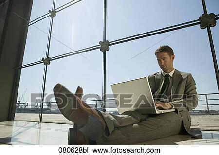 Stock Image - businessman sitting on floor in front of window working with laptop computer. Fotosearch