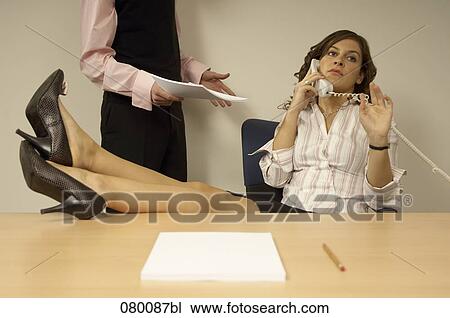 Stock Image - businesswoman talking on telephone with colleague disturbing her. Fotosearch