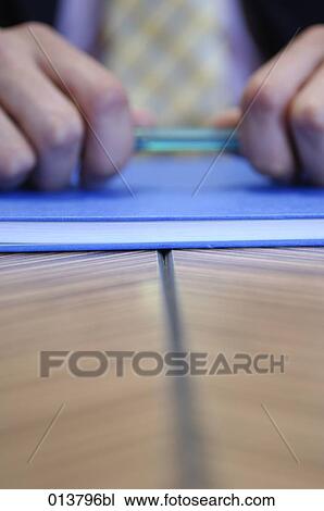 Stock Image - close-up of hands holding pen in meeting, businessman in background. Fotosearch