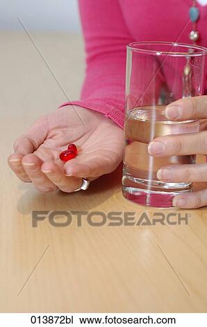 Stock Image - close-up of woman holding pills and glass of water. Fotosearch