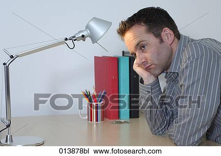 Stock Image - depressed and bored looking office worker sitting at his desk. Fotosearch