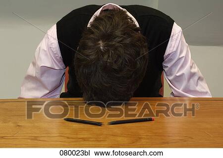 Stock Image - depressed businessman laying his head on table with broken pencil in foreground. Fotosearch
