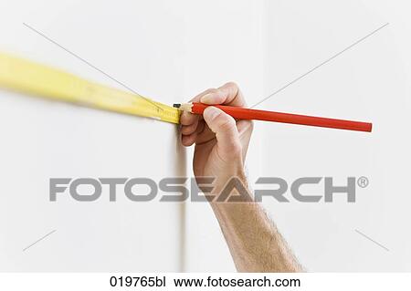 Stock Image - detail of young man making marking on the wall with folding rule and pencil. Fotosearch